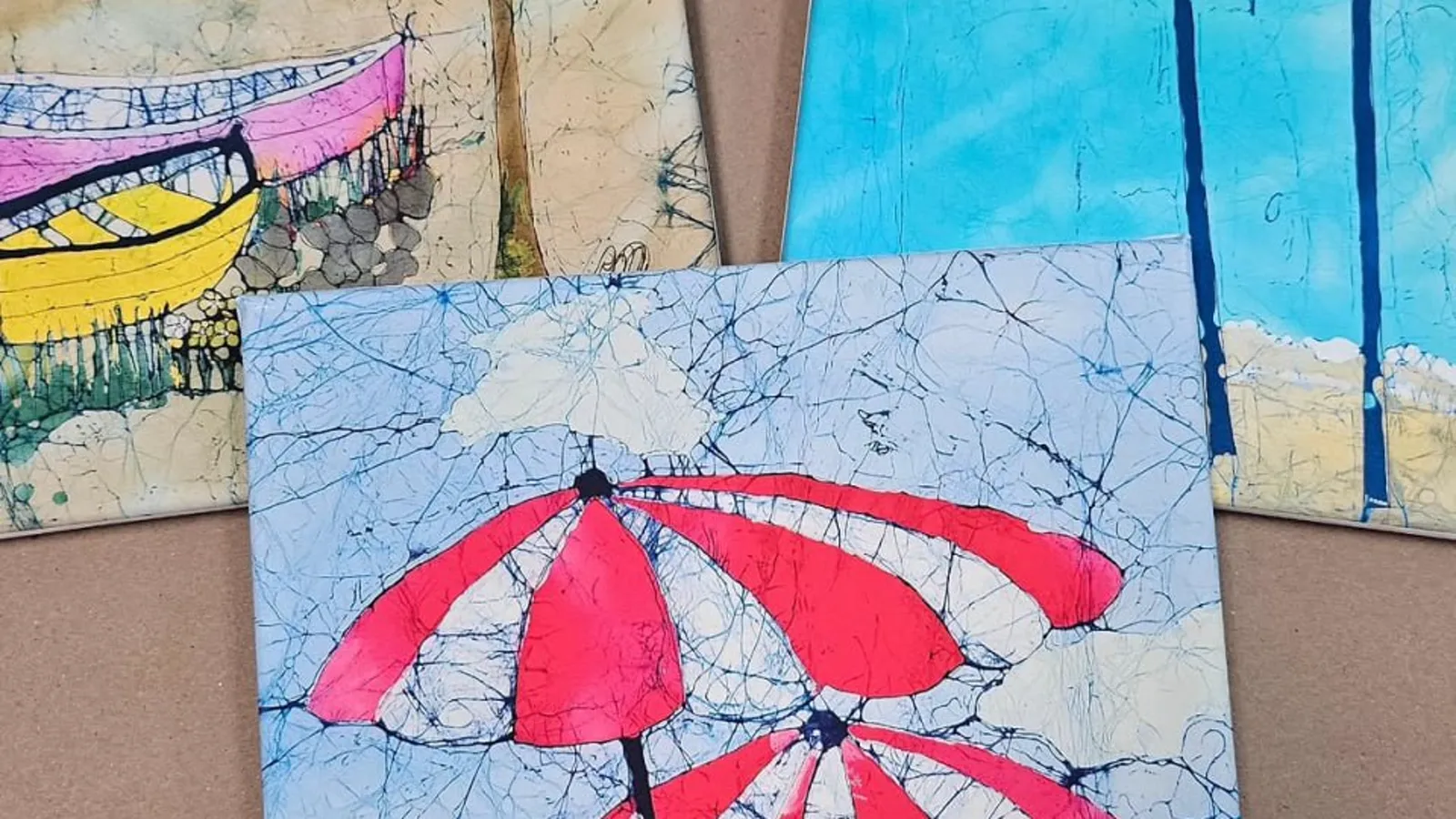 Three canvas prints of beach umbrellas and palm trees leaning against a wall.