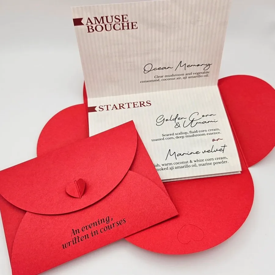 A tasting menu card standing beside a red die-cut envelope closed with a small paper heart.