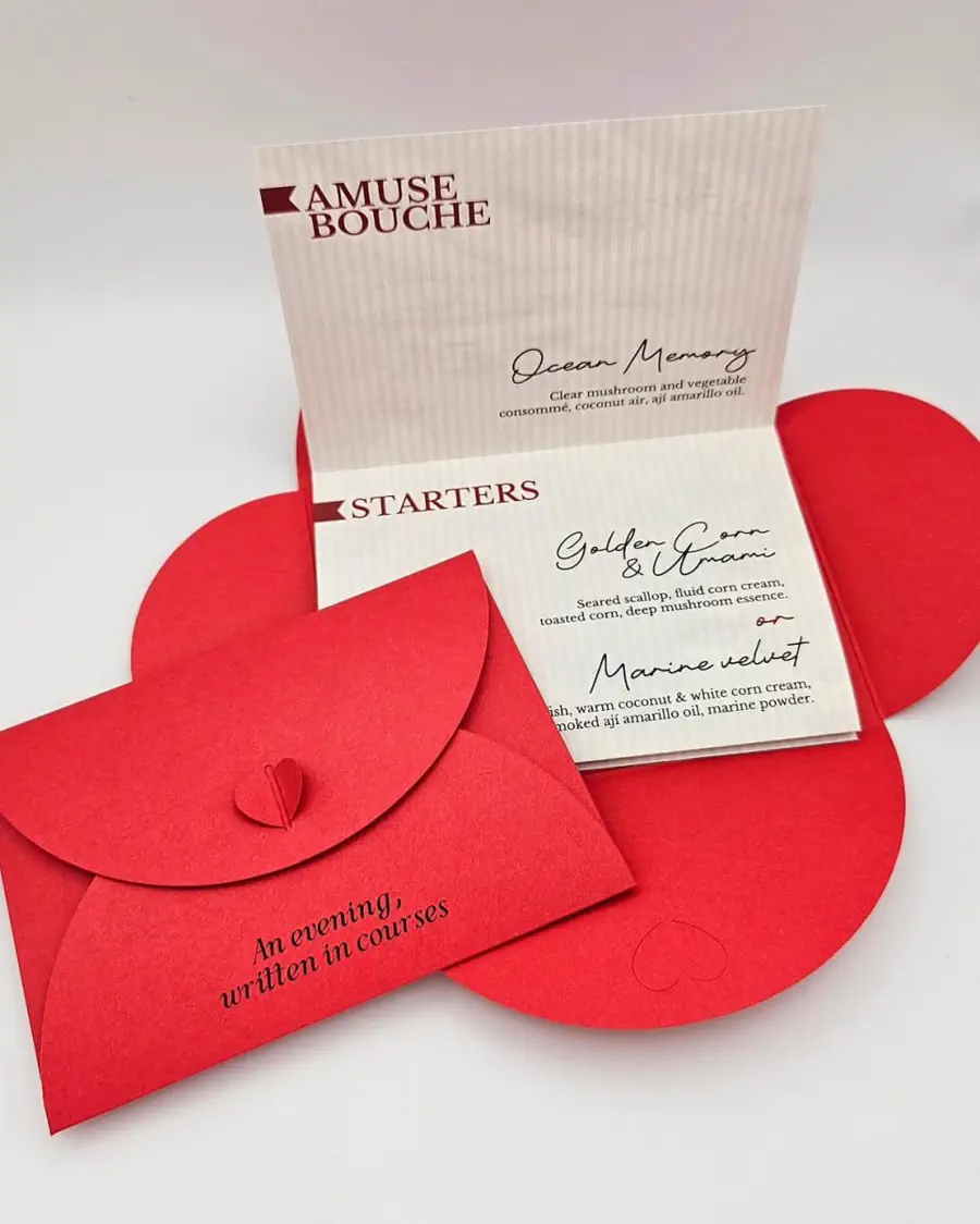 A tasting menu standing open beside a red die-cut envelope closed with a small paper heart.