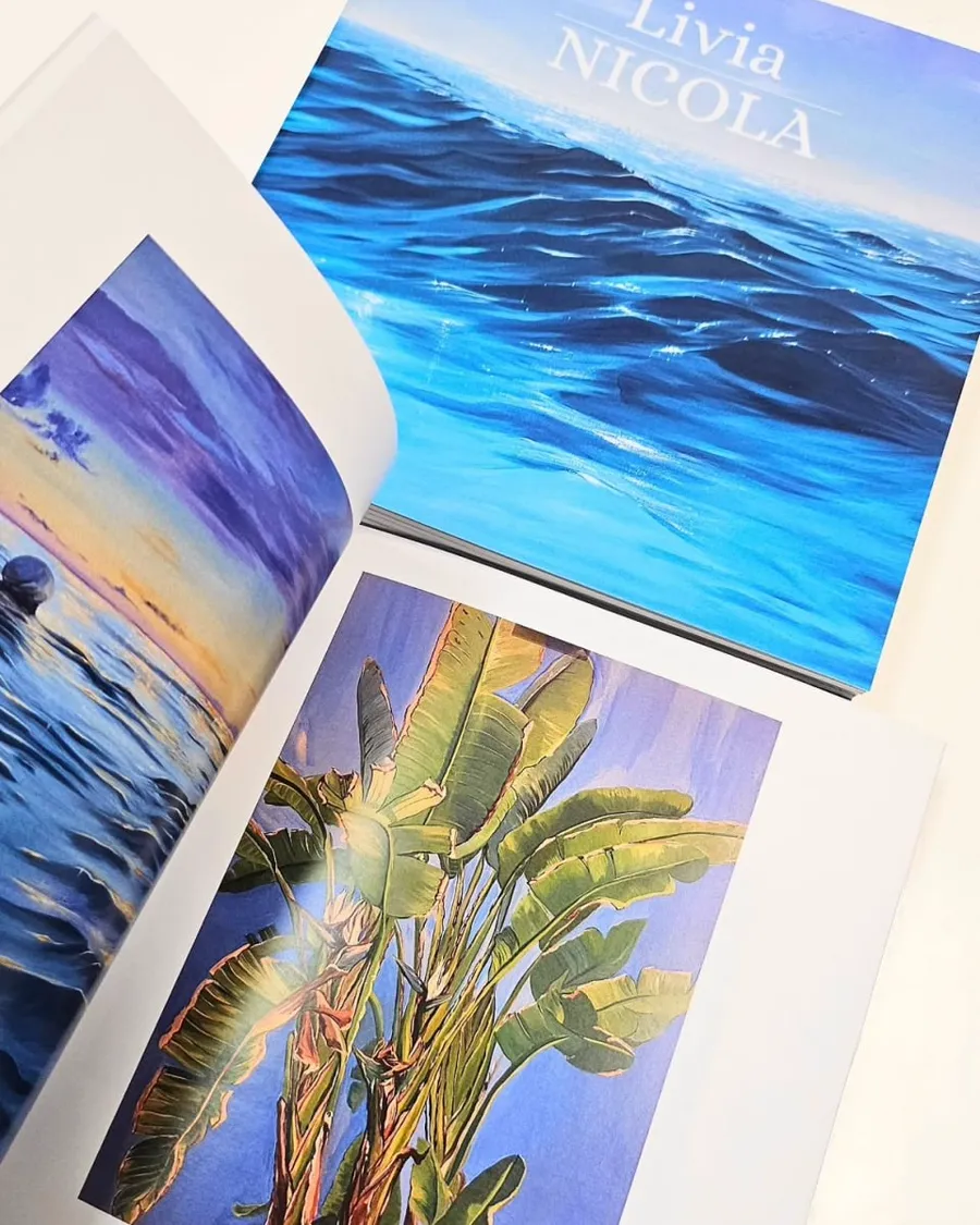 The same book opened flat beside a canvas print of a palm against a blue sky.